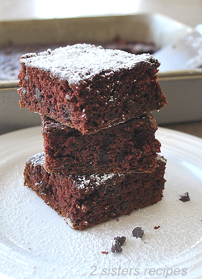  3 square brownies on top of once another on a white plate.