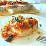 A white plate with a serving of swordfish baked with a tomato and olive sauce on top.