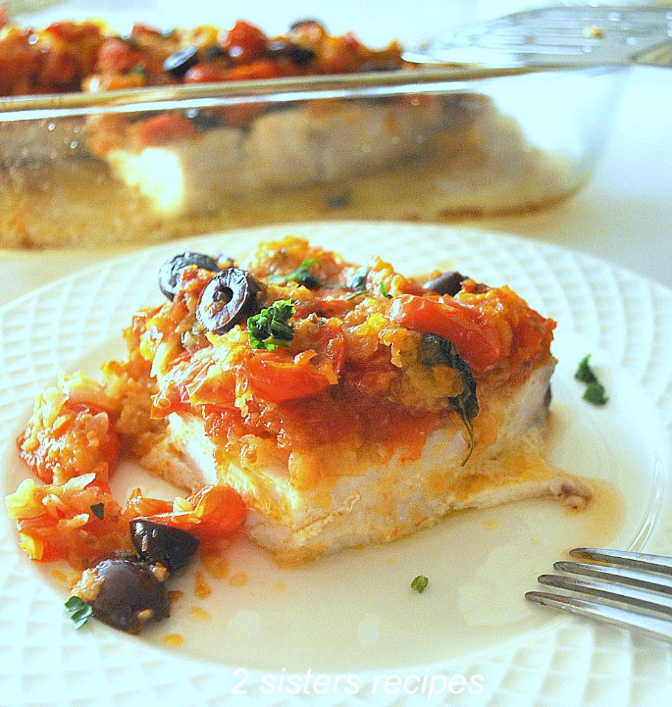 A white plate with a serving of swordfish baked with a tomato and olive sauce on top.