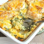 A spoon inside a white casserole dish filled with rice and chicken and spinach.