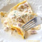 A forkful of butternut squash filled ravioli topped with a cream sauce and grated parmesan cheese.