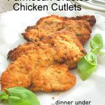 Parmesan Crusted Chicken Cutlets served on a white platter with fresh basil leaves on the side.