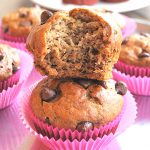 2 chocolate chip muffins with pink cup cake liners with a bite out of one.