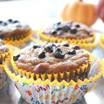 Three pumpkin muffins set on inside paper liners, and on the table.