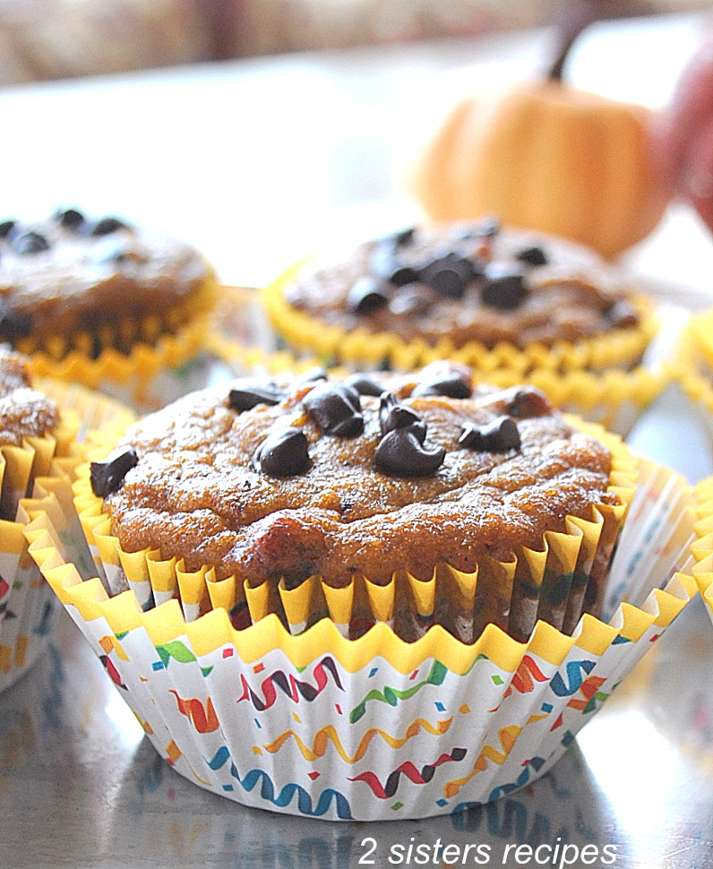 Three pumpkin muffins set on inside paper liners, and on the table.