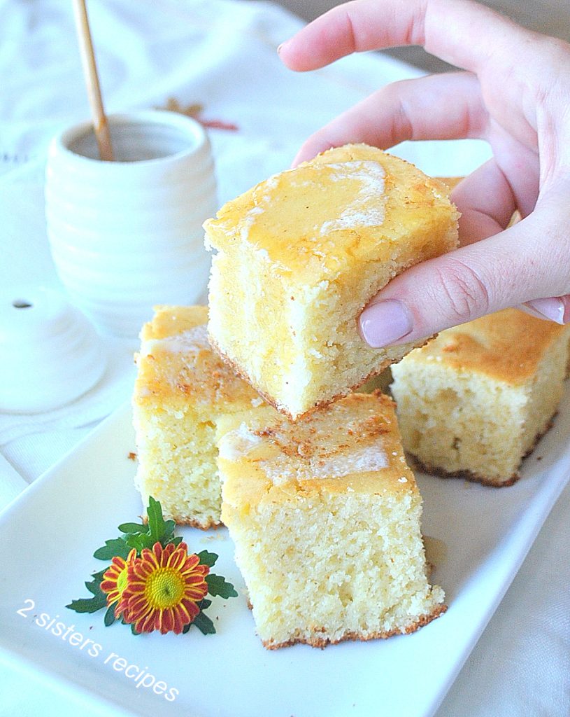 Someone's hand is pikcing up a pieces of cornbread. by 2sistersrecipes.com