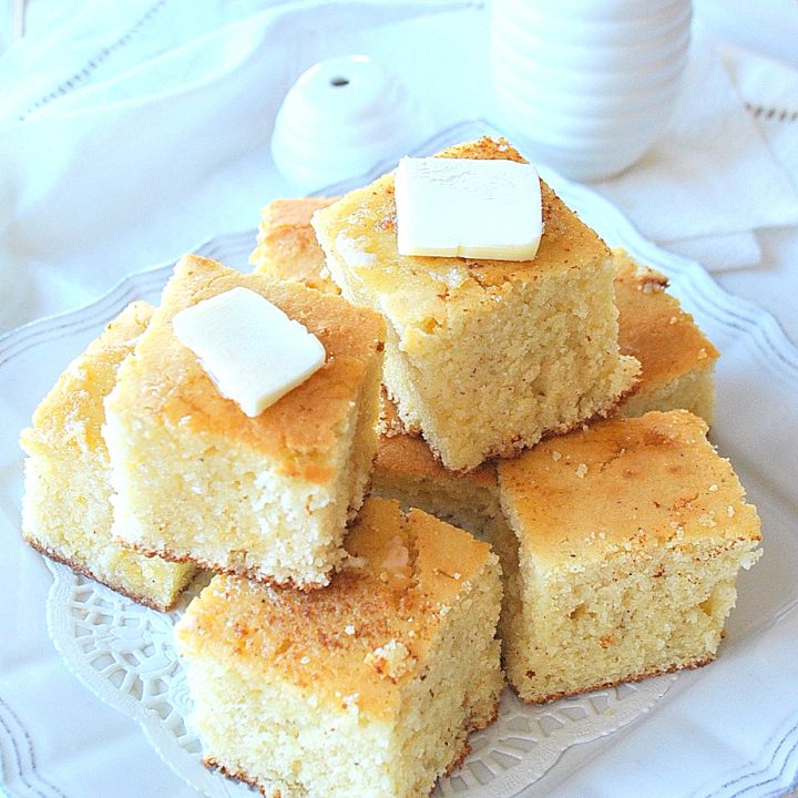 A stack of Cornbread with butter on top on a white platter. by 2sistersrecipes.com