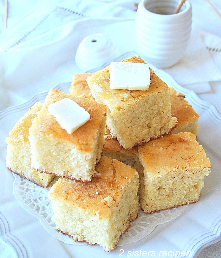 A stack of Cornbread with butter on top on a white platter. by 2sistersrecipes.com