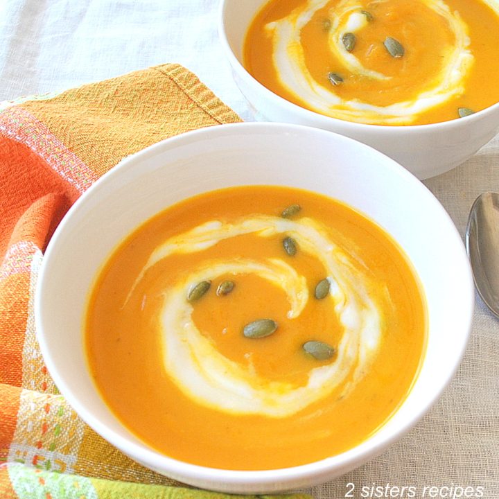 A orange colored creamy soup with a white cream swirl and pumpkin seeds on top.