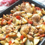A baking pan filled with sliced bake potatoes, chicken and sliced tomatoes.
