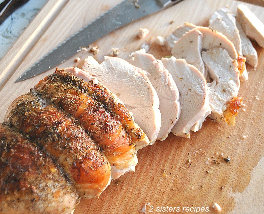 A turkey breast sliced on a wood cutting board. by 2sistersrecipes.com