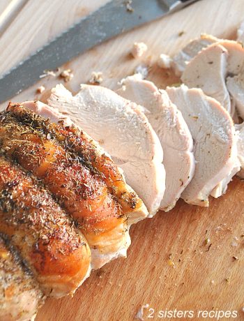 A turkey breast sliced on a wood cutting board. by 2sistersrecipes.com