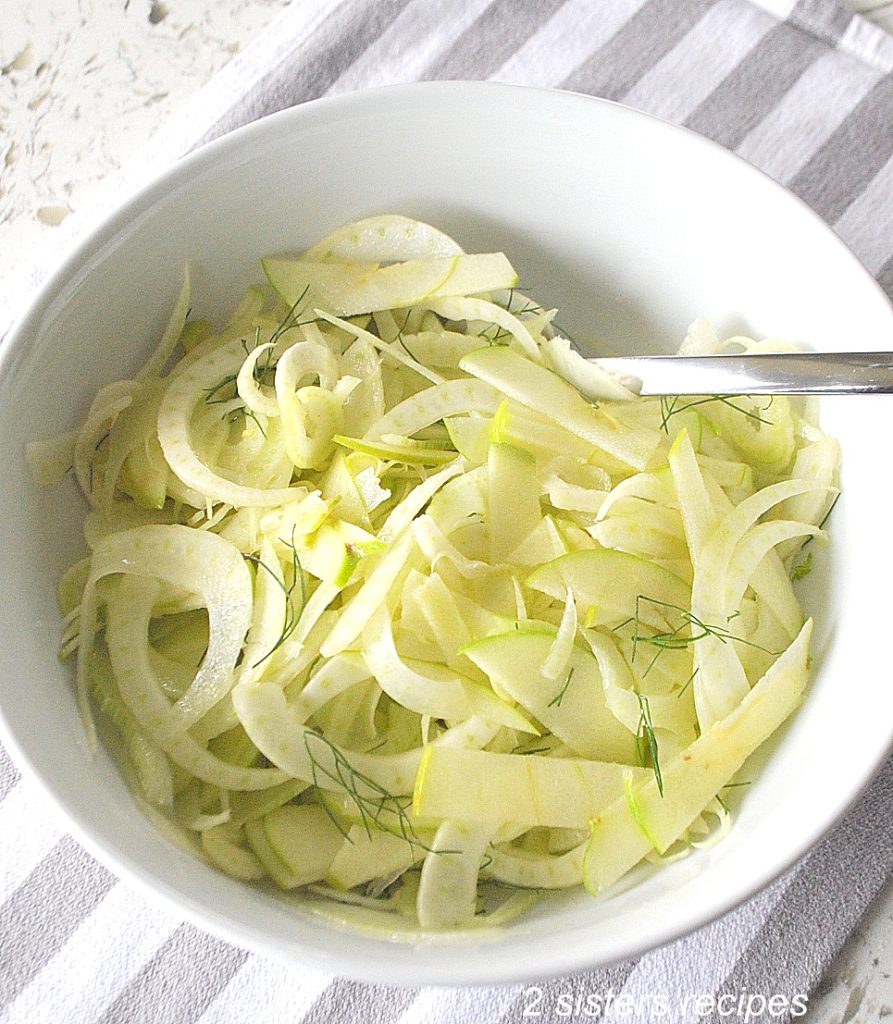 A white salad bowl with thinly sliced shavings of fennel and apples.