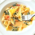 A forkful of farfalle pasta with chicken and spinach over a dish.