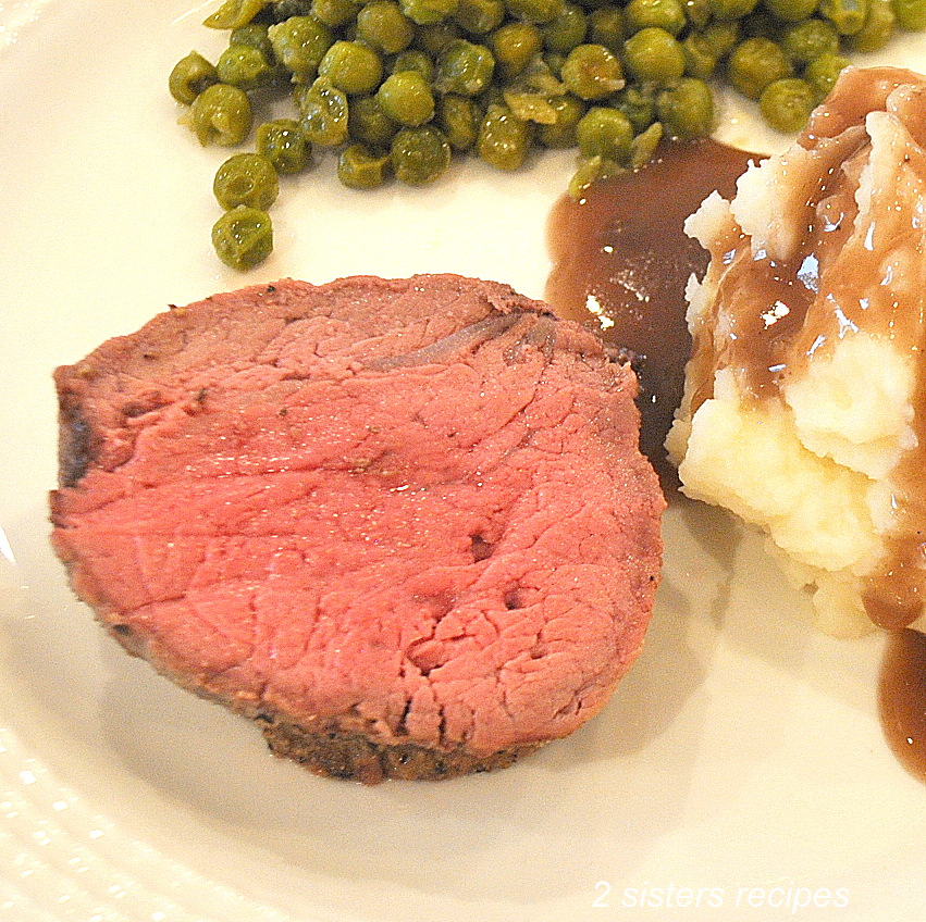 A piece of filet mignon on a white dinner plate with peas and mashed potatoes. 
