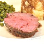 A slice of meat on a white plate with peas and mashed potatoes with gravy.