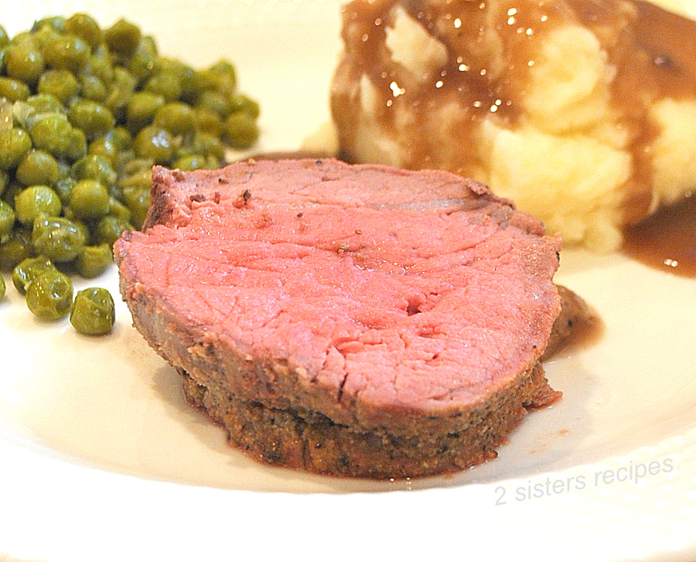A slice of cooked filet mignon on a plate with peas and mashed potatoes and gravy.
