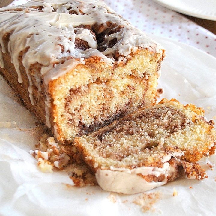 A loaf of bread with glaze on top, a sliced to see the swirl of cinnamon inside.