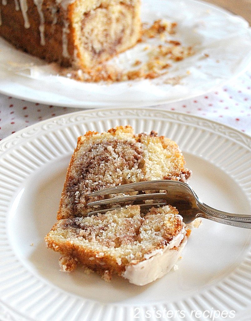  A slice of Cinnamon Swirl Quick Bread on a white plate with a fork in the center cut. by 2sistersrecipes.com