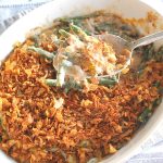 A spoonful of creamy greens beans with a crunchy topping served in a casserole baking dish.