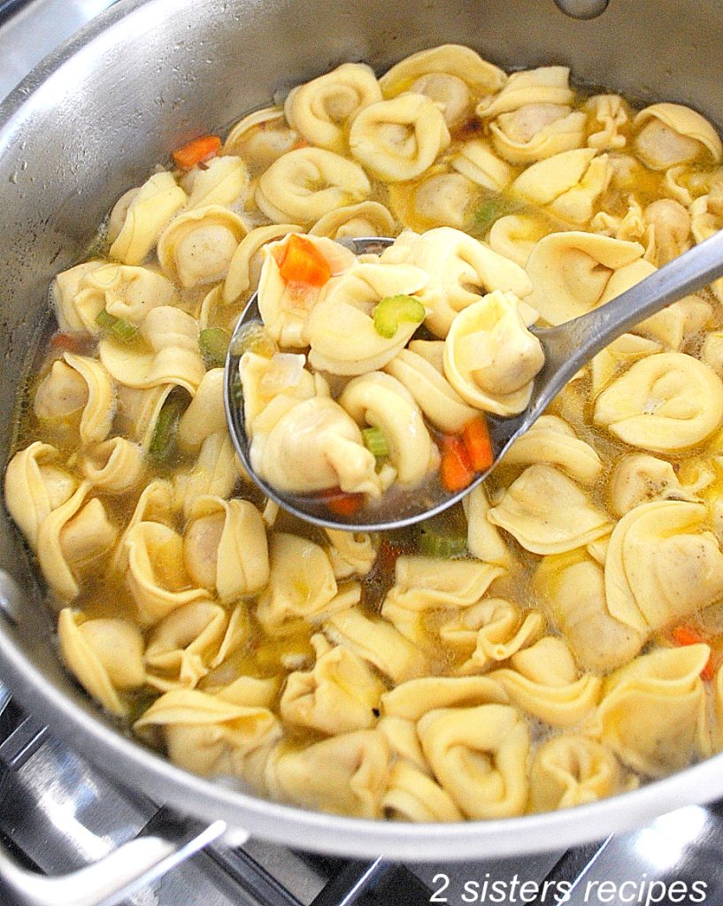 A large pot of tortellini soup and a ladle full of it. 