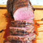 A roast carved into slices on a wood board.