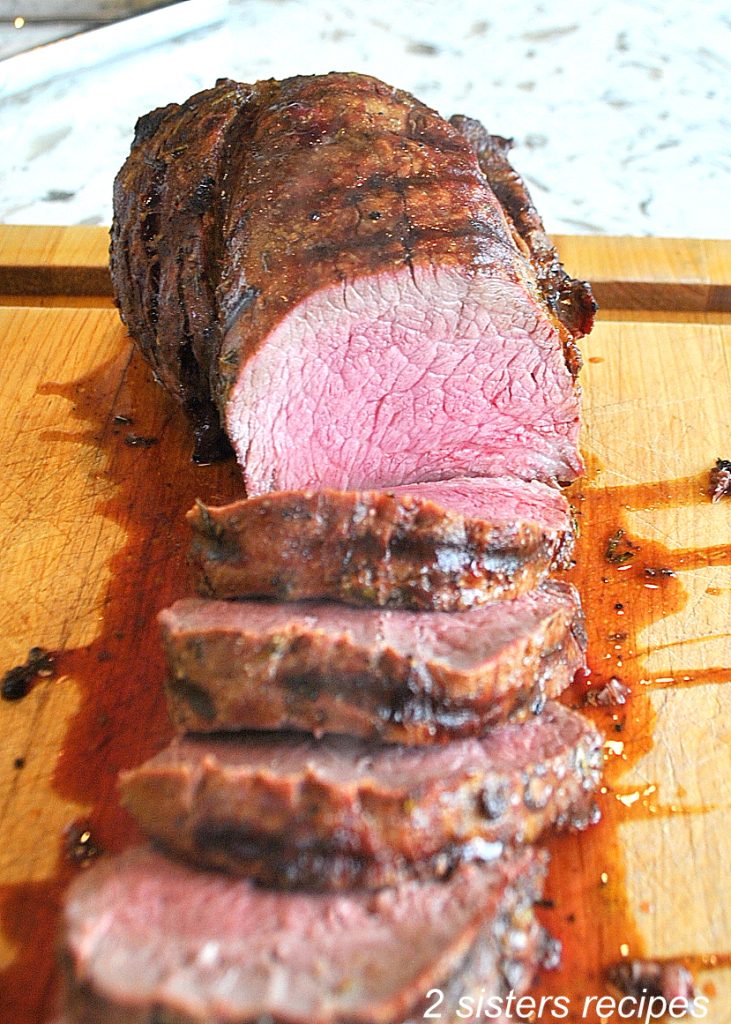 A roast carved into slices on a wood board.