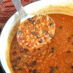 A ladle filled with cooked meat and beans over the Dutch oven pot.