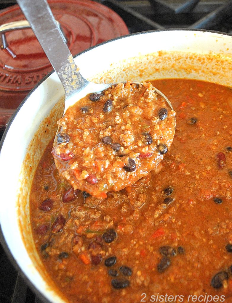 A ladle of chili over the dutch oven pot. by 2sistersrecipes.com