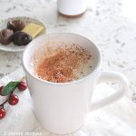 A white mug filled with brewed milk, and cocoa powder scattered on top.
