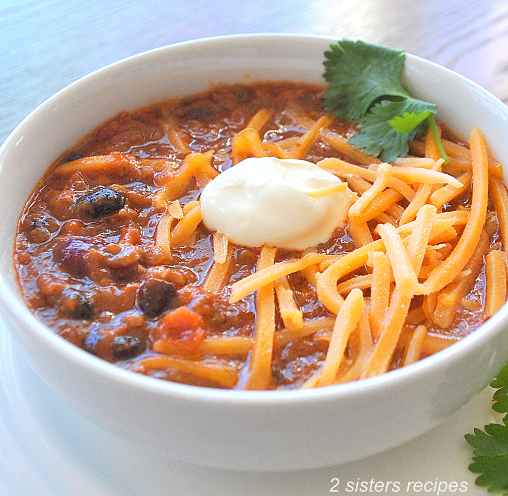 A bowl of beef chili as with beans, shredded cheese, and sour cream on top.