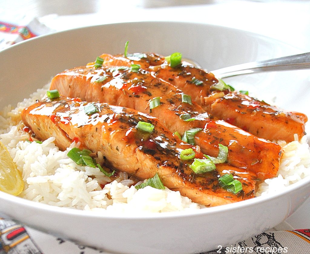 A white plate filled with steamed rice and cooked salmon steaks with green onions scattered on top.