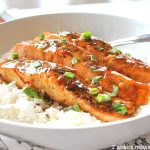 A white plate filled with steamed rice and cooked salmon steaks with green onions scattered on top.