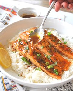 Spooning sweet chili sauce over cooked salmon and white rice in a dinner plate.