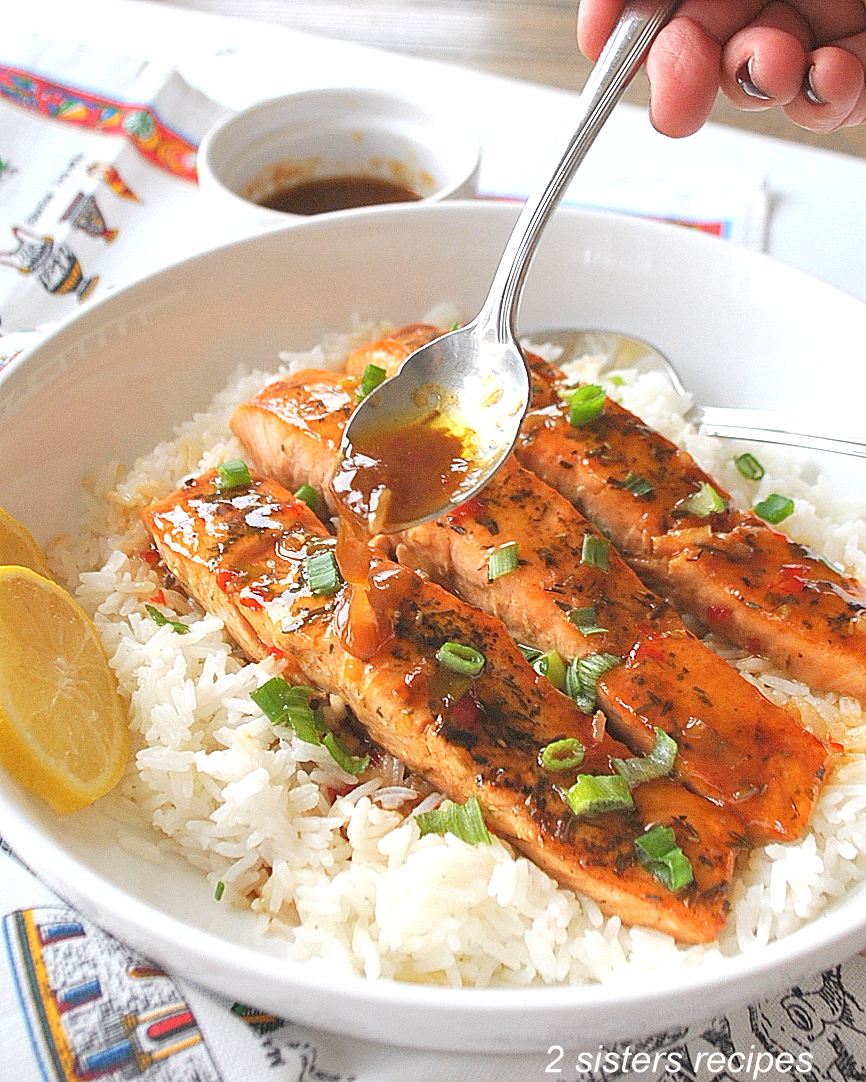 Spooning sweet chili sauce over cooked salmon and white rice in a dinner plate.