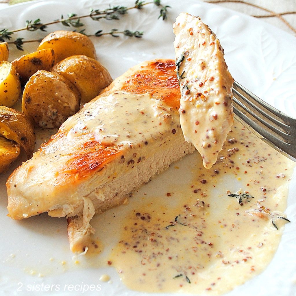 A forkful of chicken breast with a mustard sauce and some little roasted potatoes on a white dinner plate.