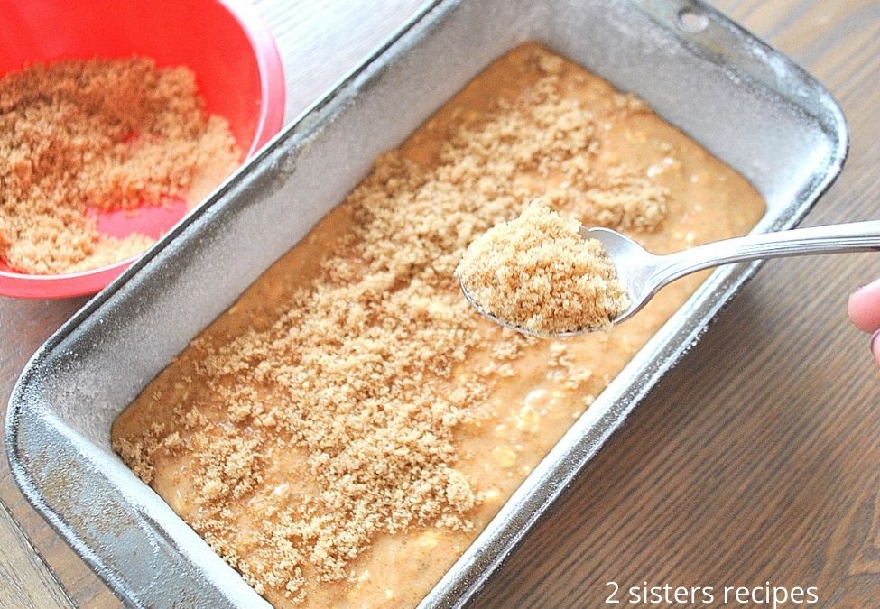 Sprinkling the cumble mixture over the batter in a loaf pan. by 2sistersrecipes.com