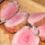 A filet mignon roast carved on a wood board.