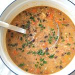 A large pot filled with black bean soup with a ladle sitting inside the pot.