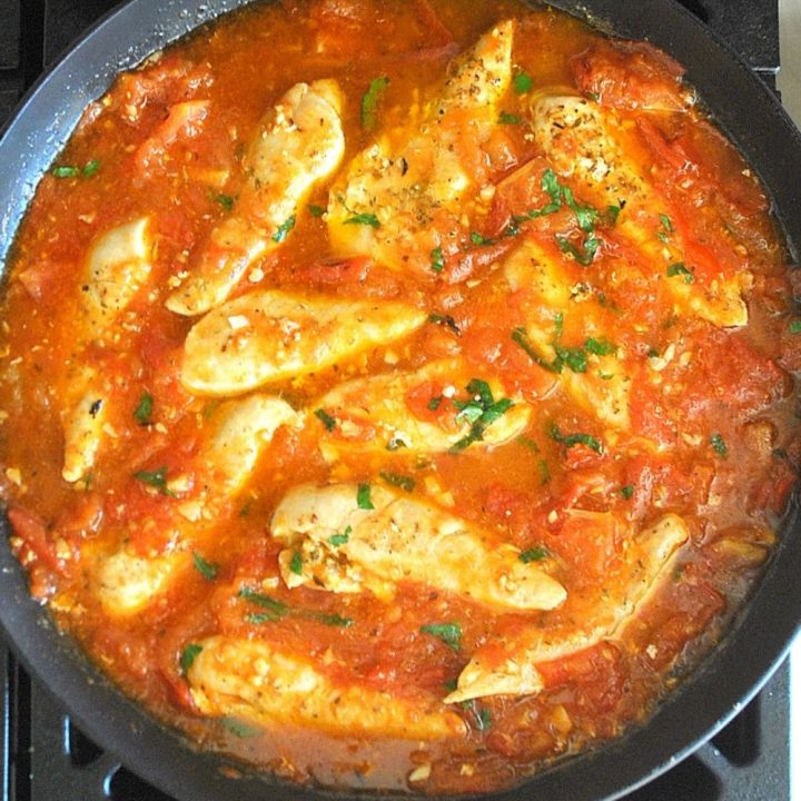 A large skillet with chicken tenders in a tomato base sauce.