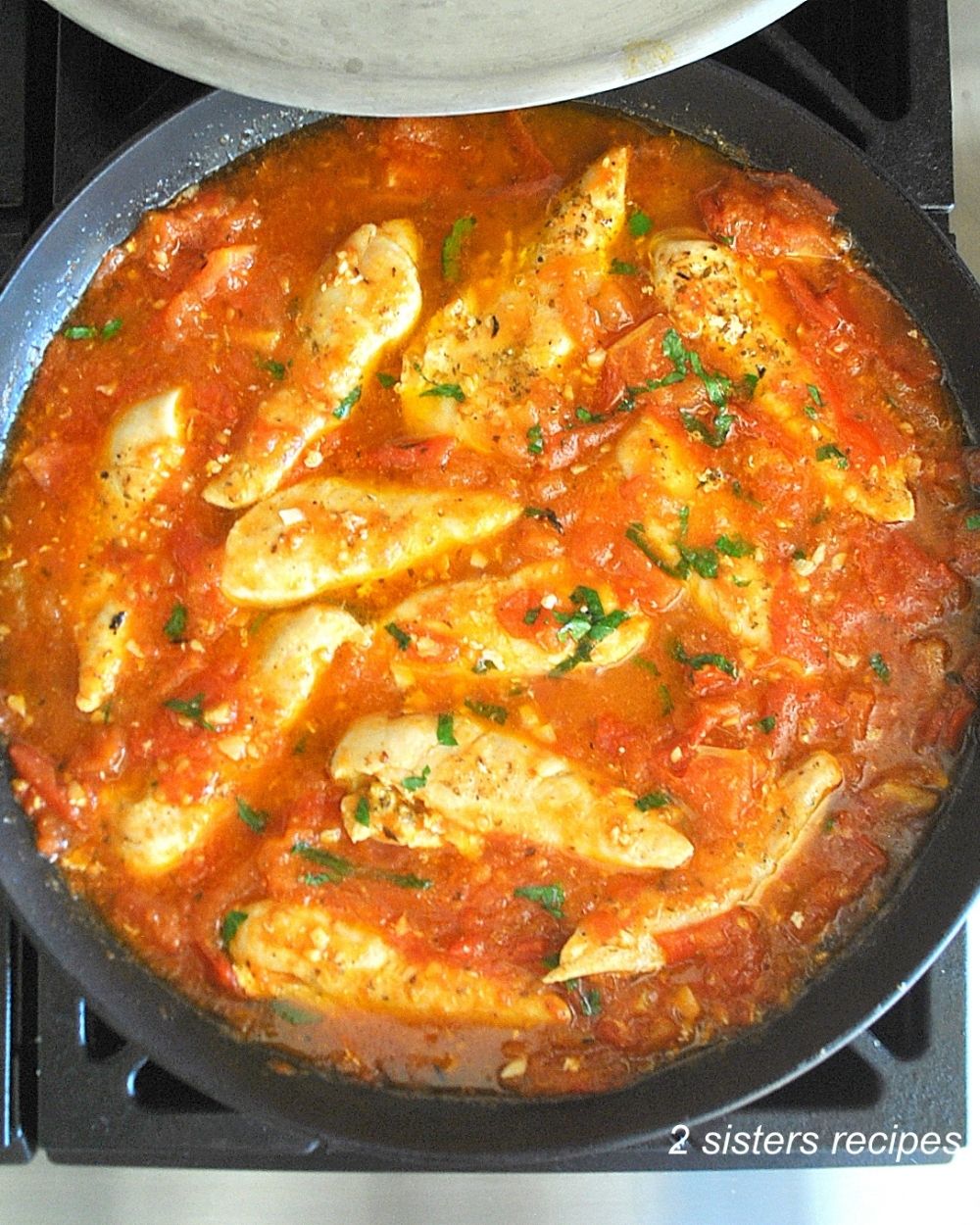 A large skillet with chicken tenders in a tomato base sauce.