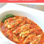 A white oval platter filled with chicken tenders cooked in tomato sauce.