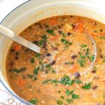 A large pot filled with Black Bean and Quinoa Soup and a ladle inside the pot.