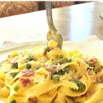 a forkful twirling some pappardelle pasta with peas and prosciutto on a white plate.