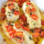 Baked cod in a white ceramic baking dish with cherry tomatoes.