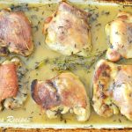 A baking dish filled with cooked chicken thighs in lemon and Thyme sauce.