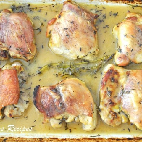 A baking dish filled with cooked chicken thighs in lemon and Thyme sauce.