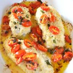 Baked cod with cherry tomatoes in a white baking dish.