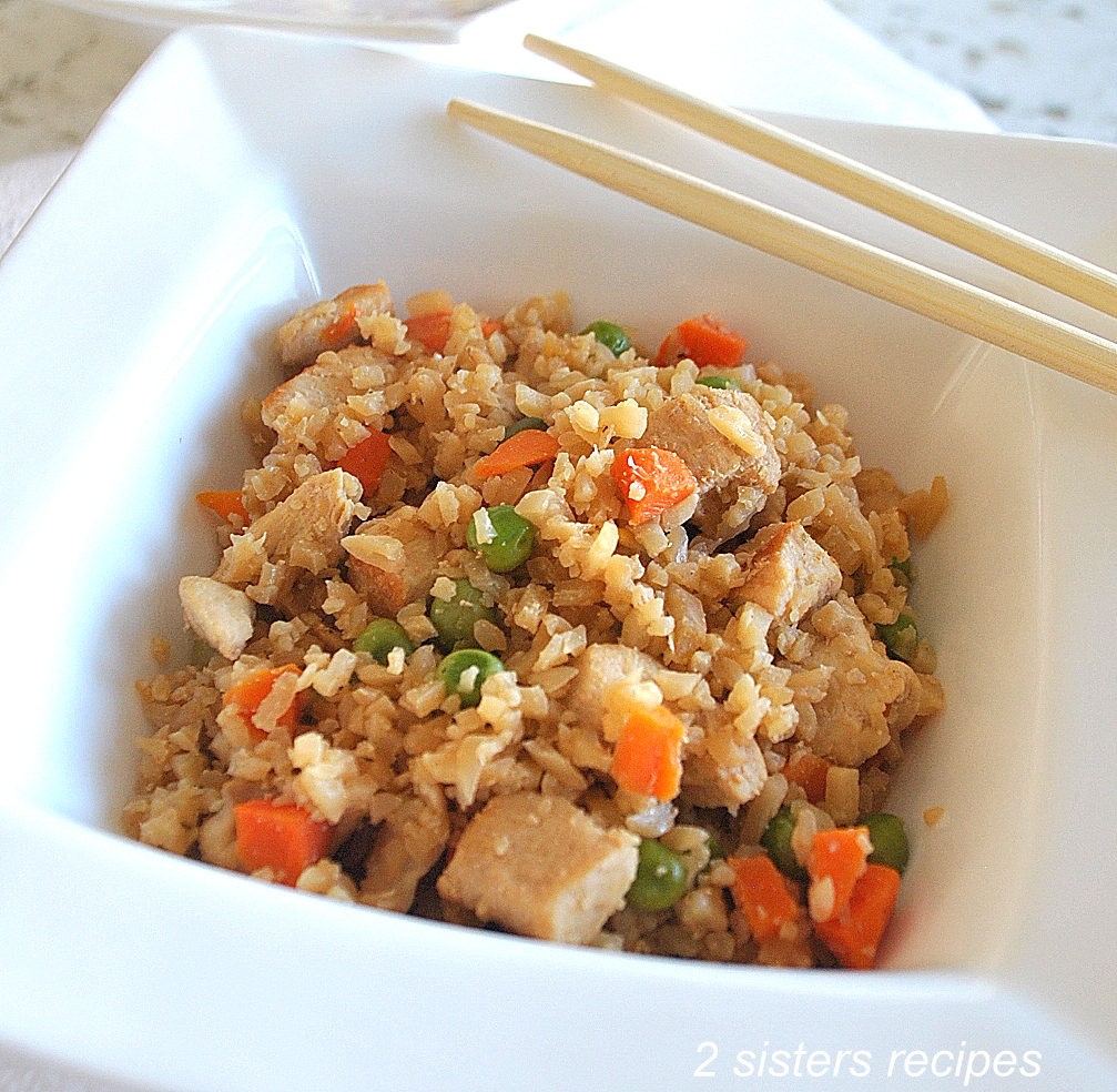 A bowl of rice and pieces of chicken and veggies with chop sticks.