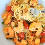 A forkful of spaghetti with shrimp and cherry tomatoes served in a white pasta bowl.